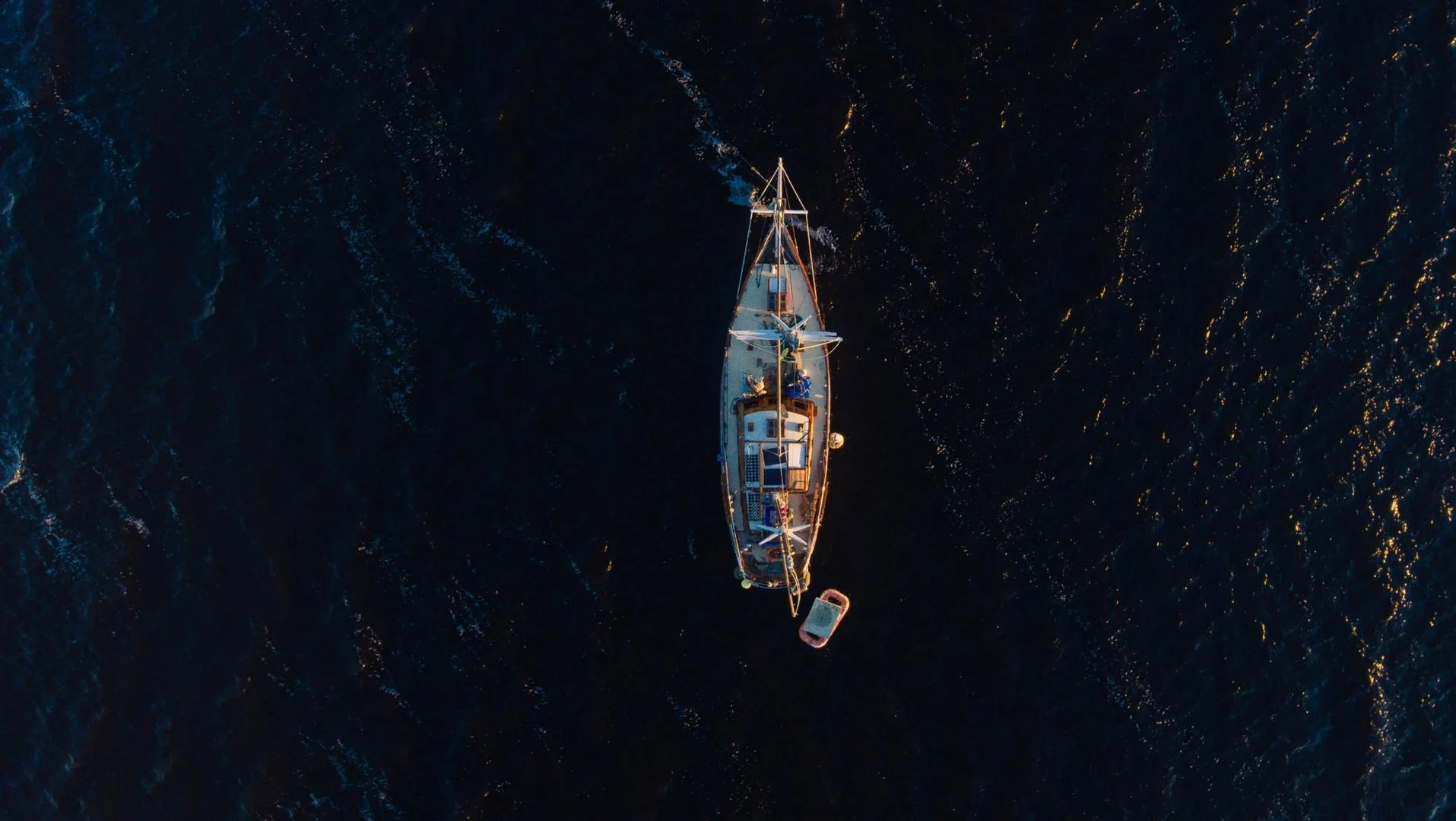 A sailing boat seen from above on deep blue water with warm evening reflections